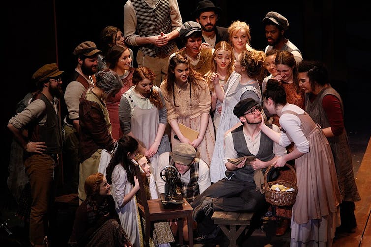 A group of people in 19th century clothing gathers around a smiling couple.